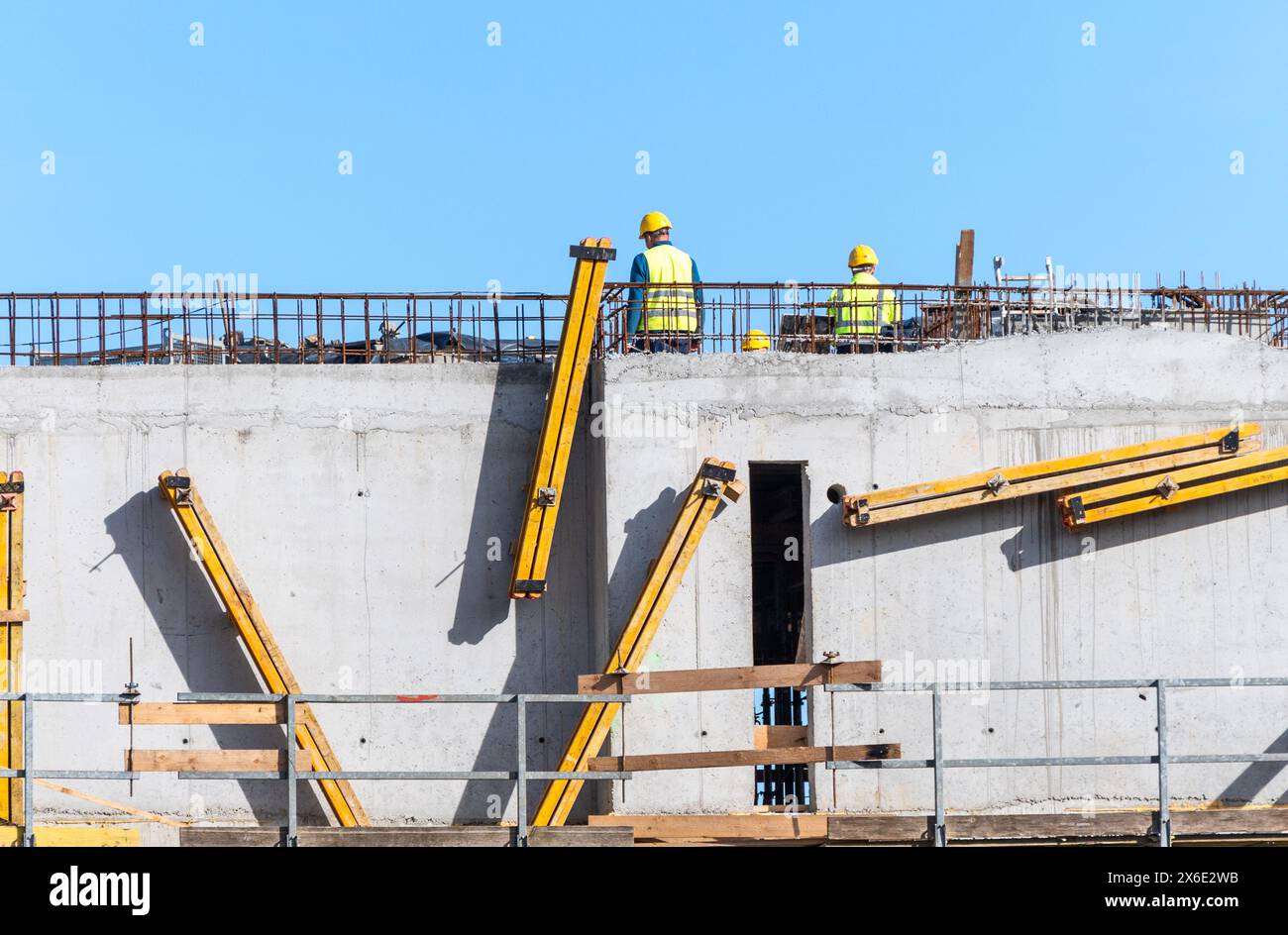Construction workers collaborating on concrete building structure under clear sky Stock Photo