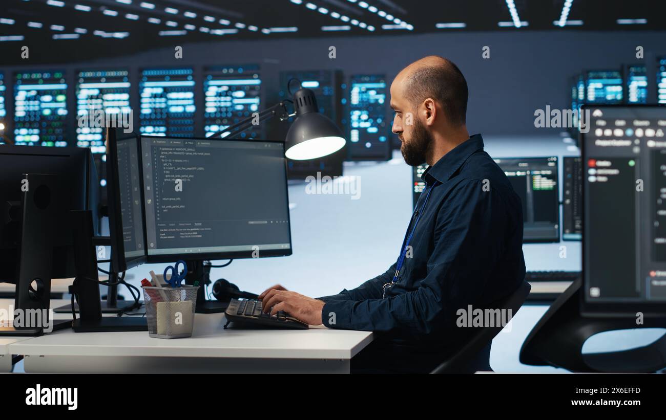 IT engineer programming in server hub housing advanced equipment storing massive datasets. Technician typing code on computer to mend data center racks doing complex computational operations Stock Photo