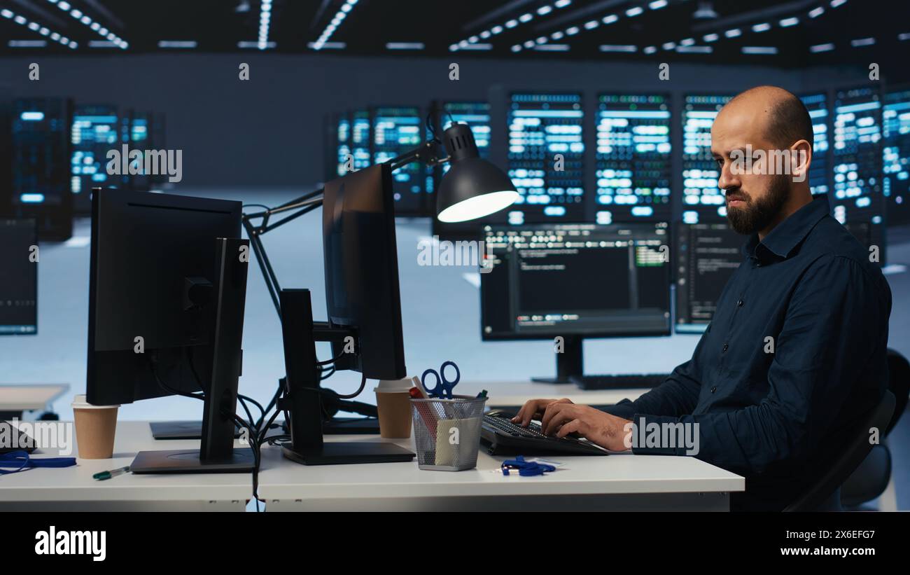 System admin focused on programming in server farm housing advanced equipment storing massive datasets. Developer typing code on PC to mend data center racks doing complex computational operations Stock Photo