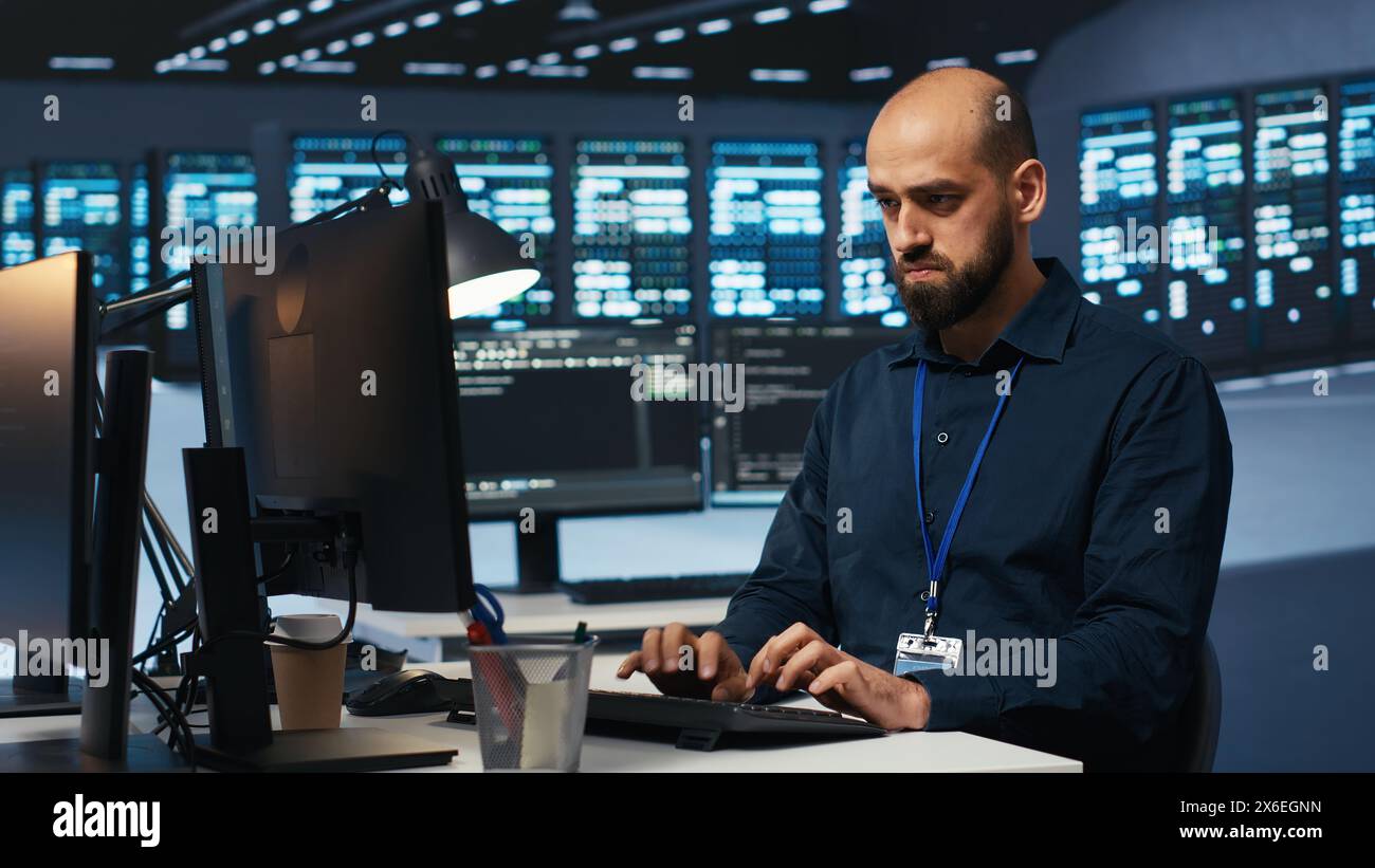 System operator overseeing server room, typing code on desktop PC ...