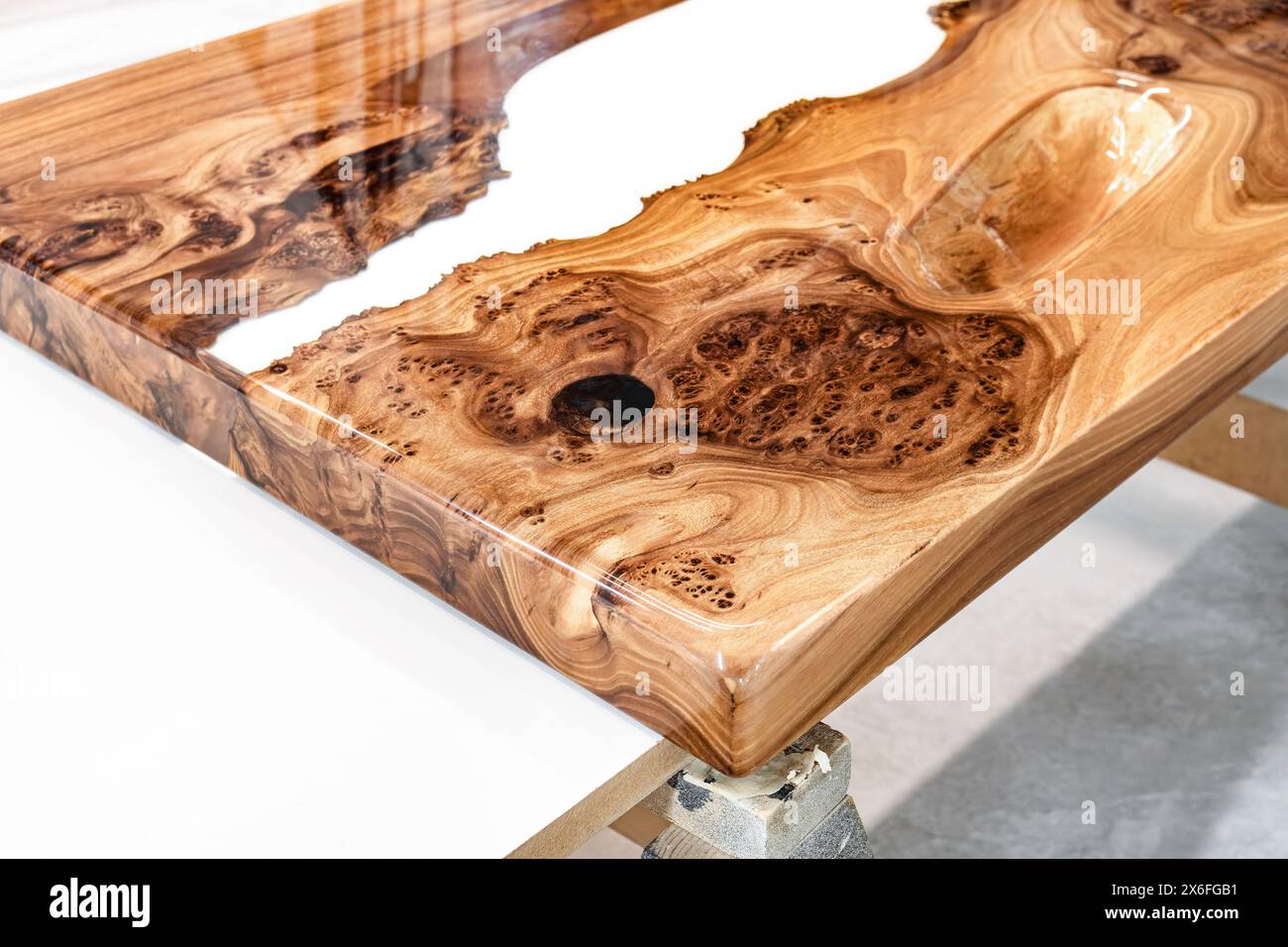 Live edge elm burl slab table top with central epoxy resin river on sawhorses in professional workshop close view Stock Photo