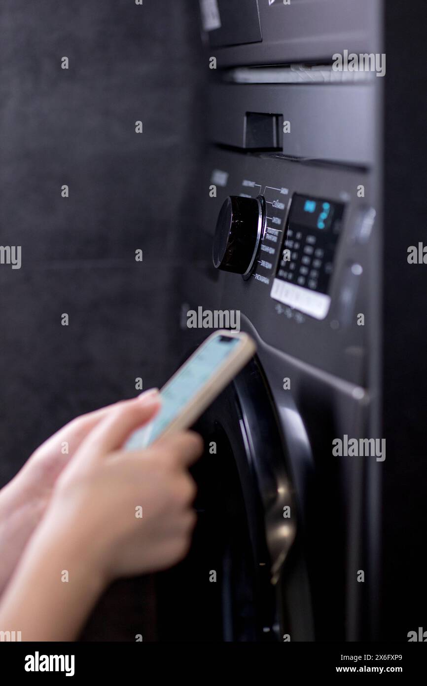 Woman controls washing machine with a phone. Stock Photo