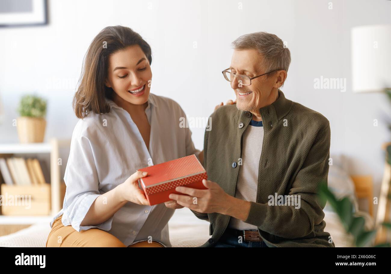 Beautiful young woman congratulating father and giving to him a gift. Stock Photo