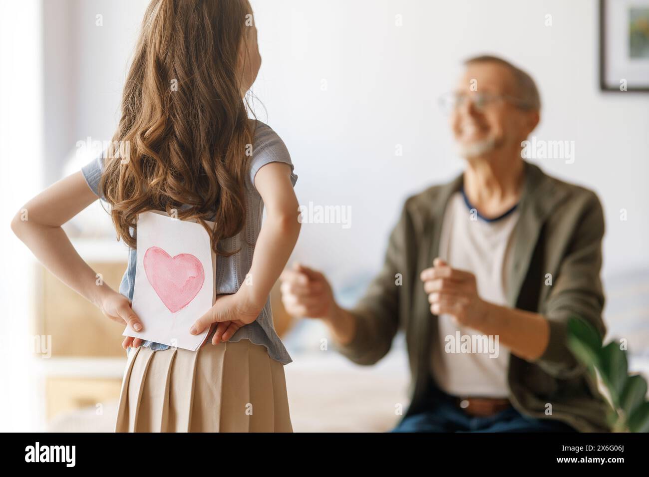 Child granddaughter is congratulating her grandfather and giving him postcard. Family holiday and togetherness. Stock Photo