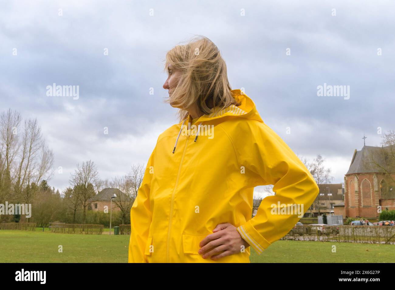 Portrait of a young woman dressed in a yellow raincoat posing with a hoody Cloudy dark sky. Caucasian Stock Photo