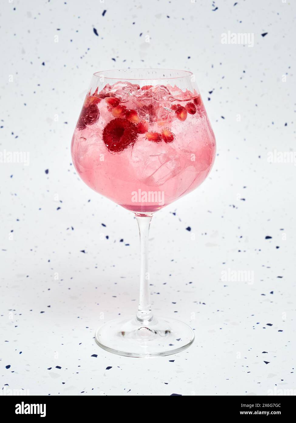 Close-Up of Refreshing Pink Gin Tonic with Berries against a speckled background Stock Photo