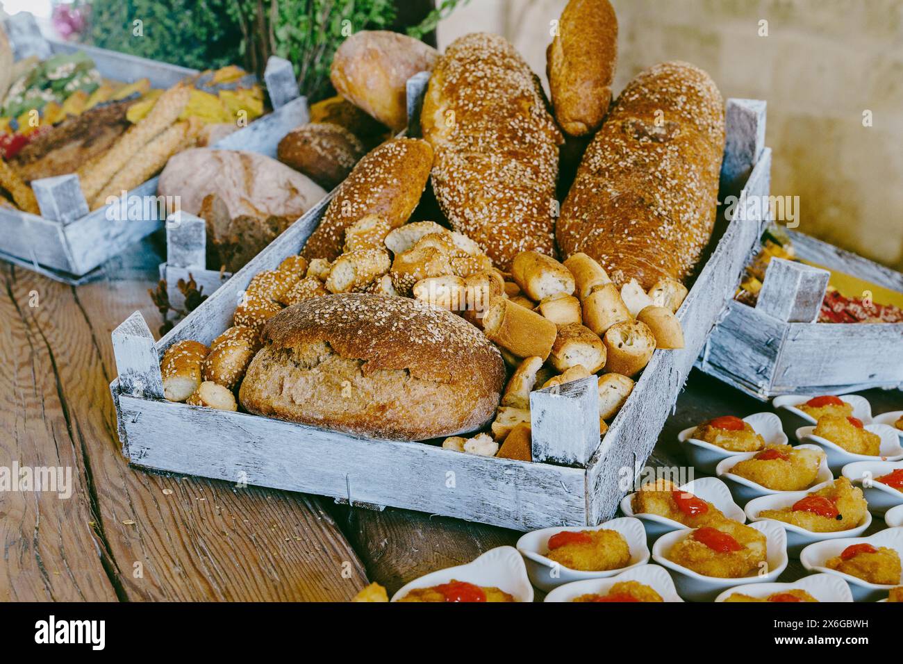 Assortment of rustic bread and gourmet appetizers displayed in wooden crates, beautifully arranged on a wooden table, showcasing a bakery product pres Stock Photo