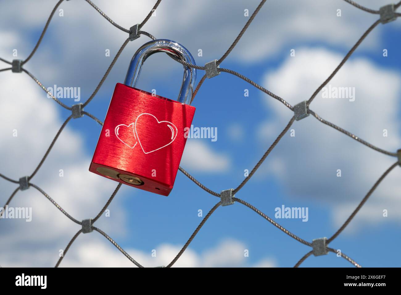 a single red love lock with two hearts hangs on a bridge railing Stock Photo