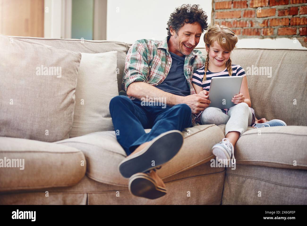 Happy, dad and girl with tablet in sofa at home for elearning, child development and knowledge with growth. Parent, kid and support with help Stock Photo