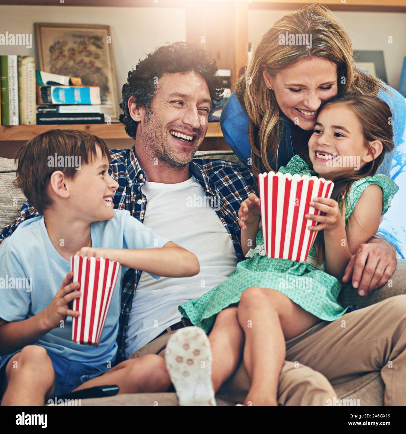 Happy family, relax and laughing with popcorn on sofa for funny movie, weekend or holiday in living room at home. Mom, dad and children with smile for Stock Photo