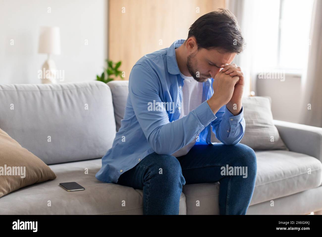 Man Sitting on Couch With Hands on Face Stock Photo