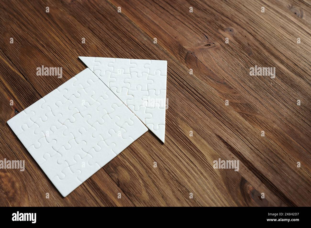 Close-up of a flat house made from jigsaw puzzle pieces isolated on wooden background with copy-space. Stock Photo