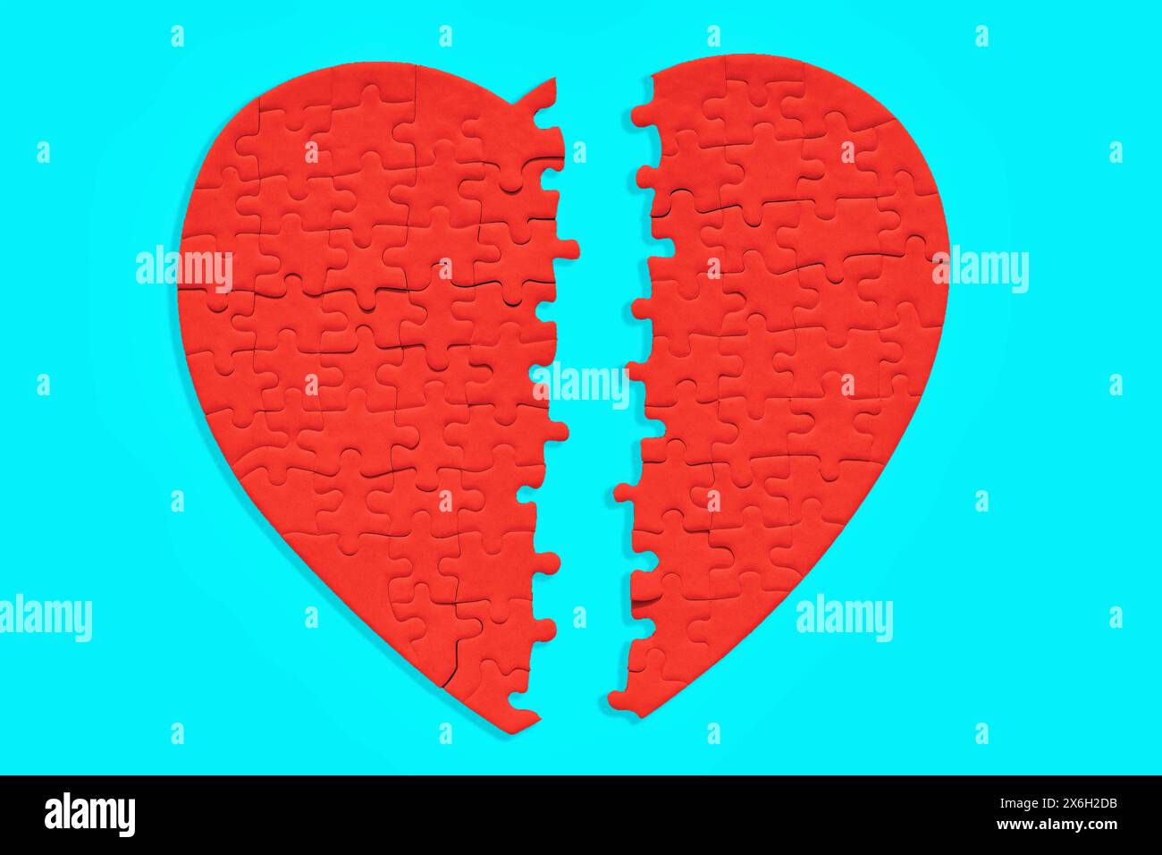 Split red heart jigsaw puzzle, zoomed in, on a light blue background. Relationships difficulties related concept. Stock Photo