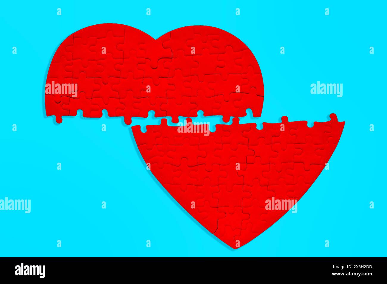 Red heart-shaped puzzle, halved and laid on a light blue surface. The fragmented pieces symbolize emotional disconnection or fractured relationships. Stock Photo