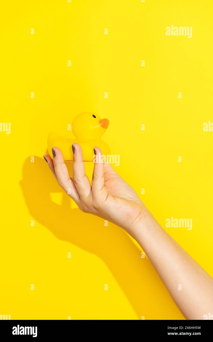 Hand holding yellow rubber duck on yellow background Stock Photo