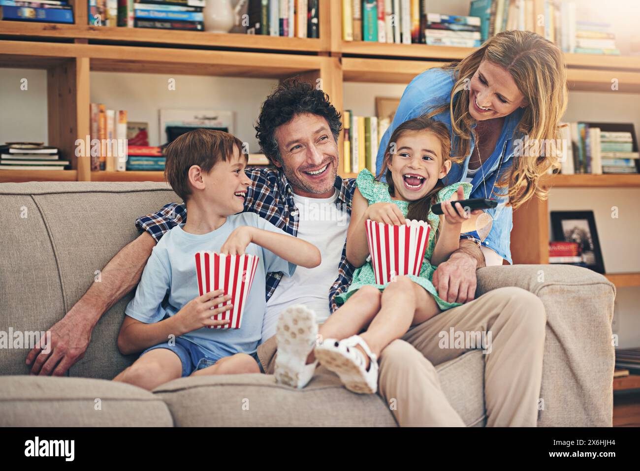 Happy family, relax and laughing with popcorn for comedy movie, weekend or holiday on living room sofa at home. Mom, dad and young children with smile Stock Photo