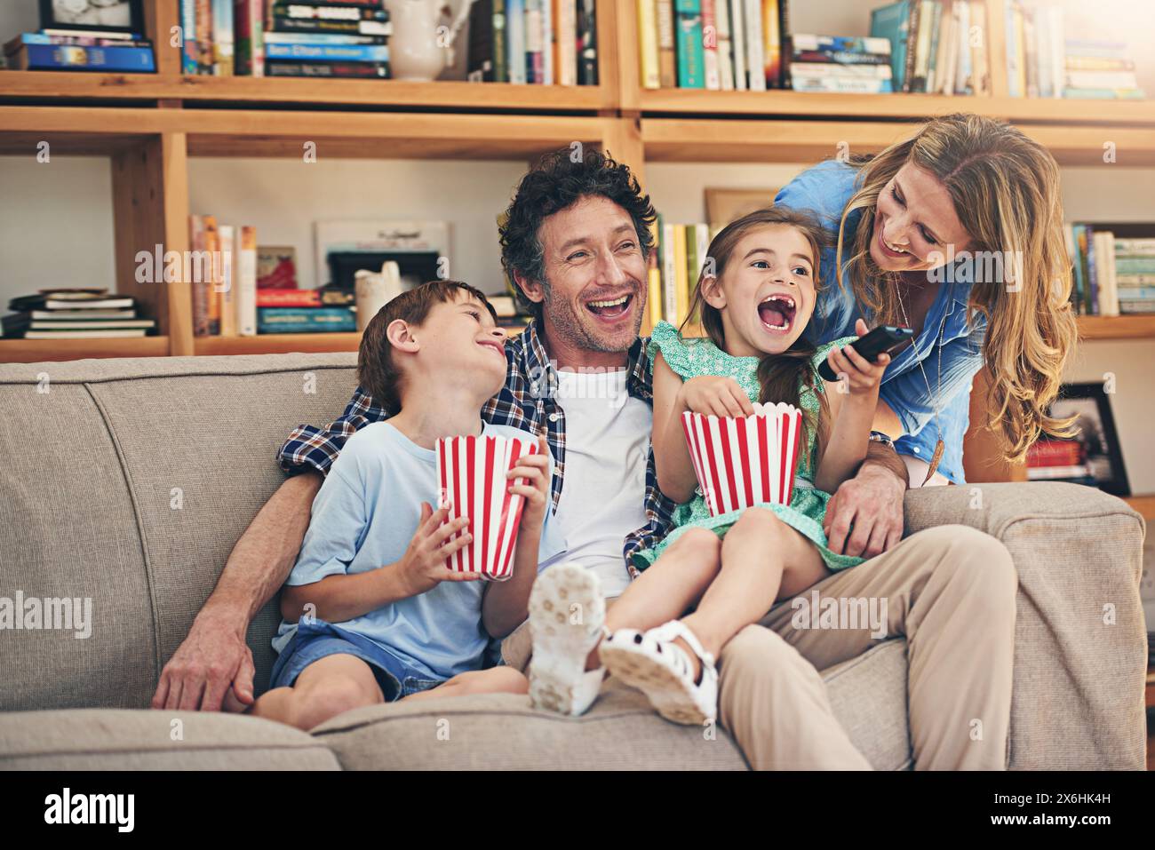 Happy family, relax and laughing with popcorn for funny movie, weekend or holiday on living room sofa at home. Mom, dad and young children with smile Stock Photo