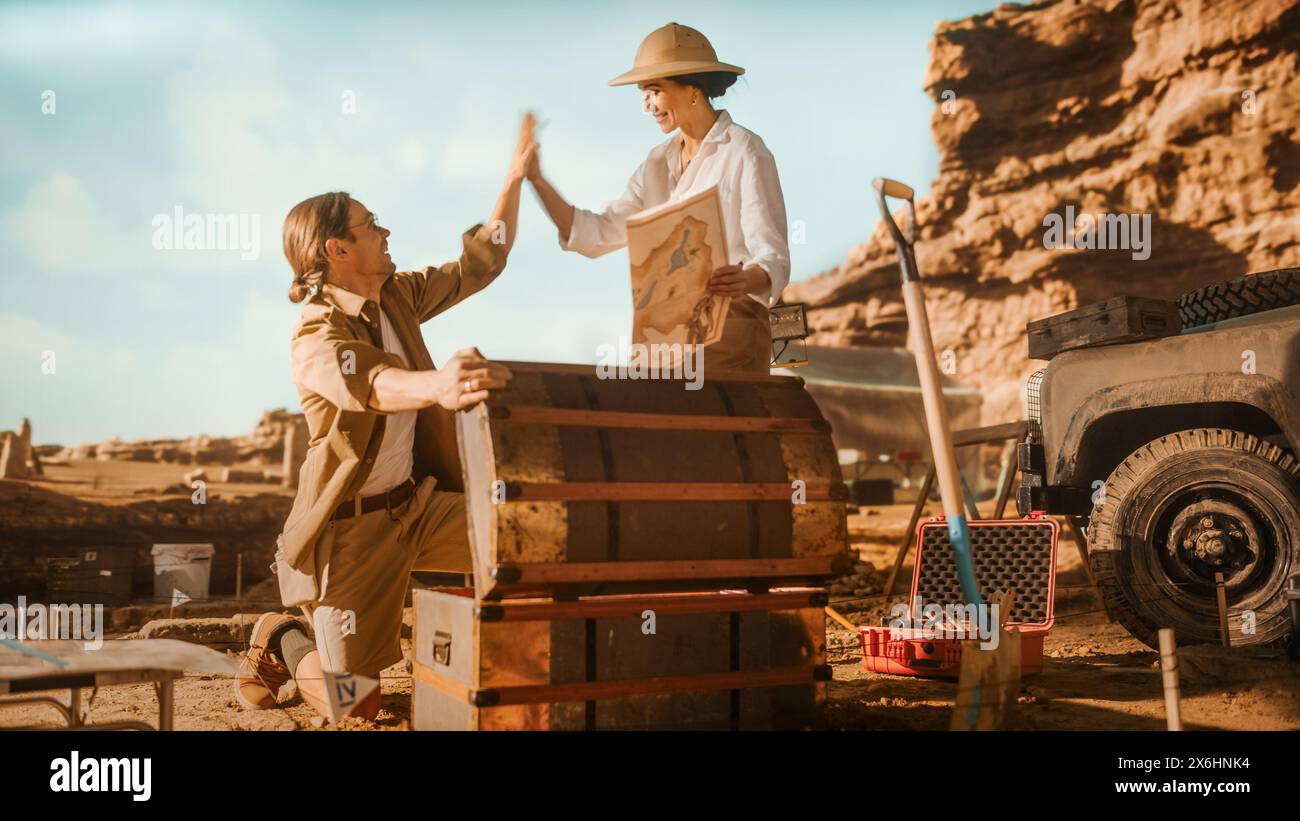 Archaeological Digging Site: Two Great Adventurers on Treasure Hunt Open Chest with Unspeakable Treasures, Celebrates Their Succers by doing High-Five. Ancient Civilization Hidden Gold Found Stock Photo