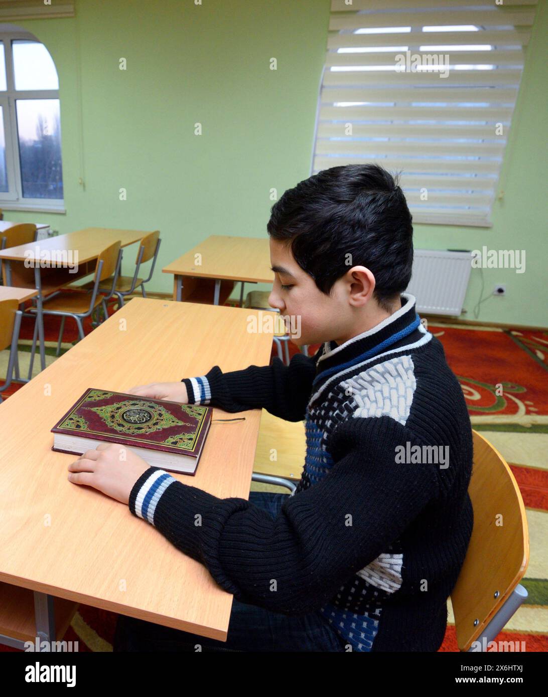 Classroom of the medrese. Muslim boy sitting at a school desk, Quran placed in front of him. October 21, 2018. Islamic culture centre, Kiev, Ukraine Stock Photo