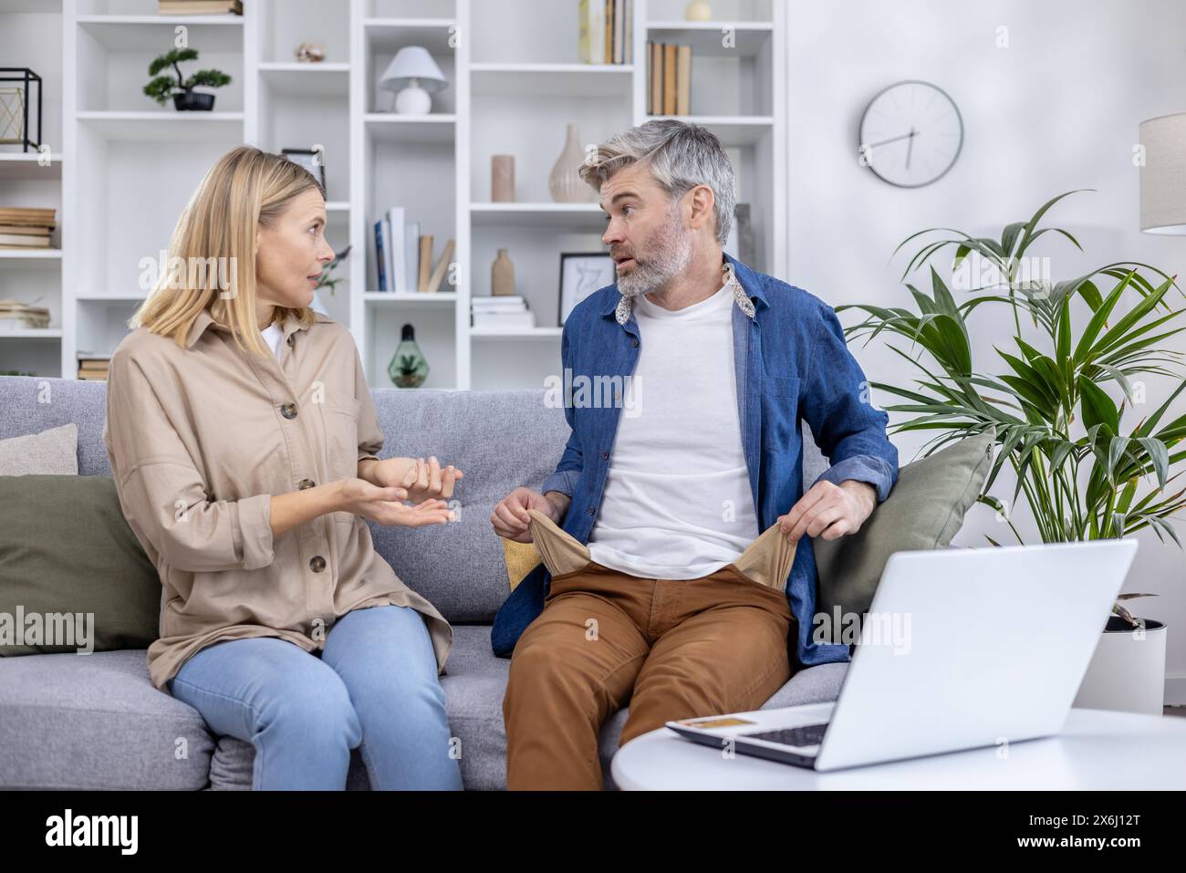 Middle-aged couple engaged in a serious conversation about financial issues, sitting on a cozy sofa in their living room. Stock Photo