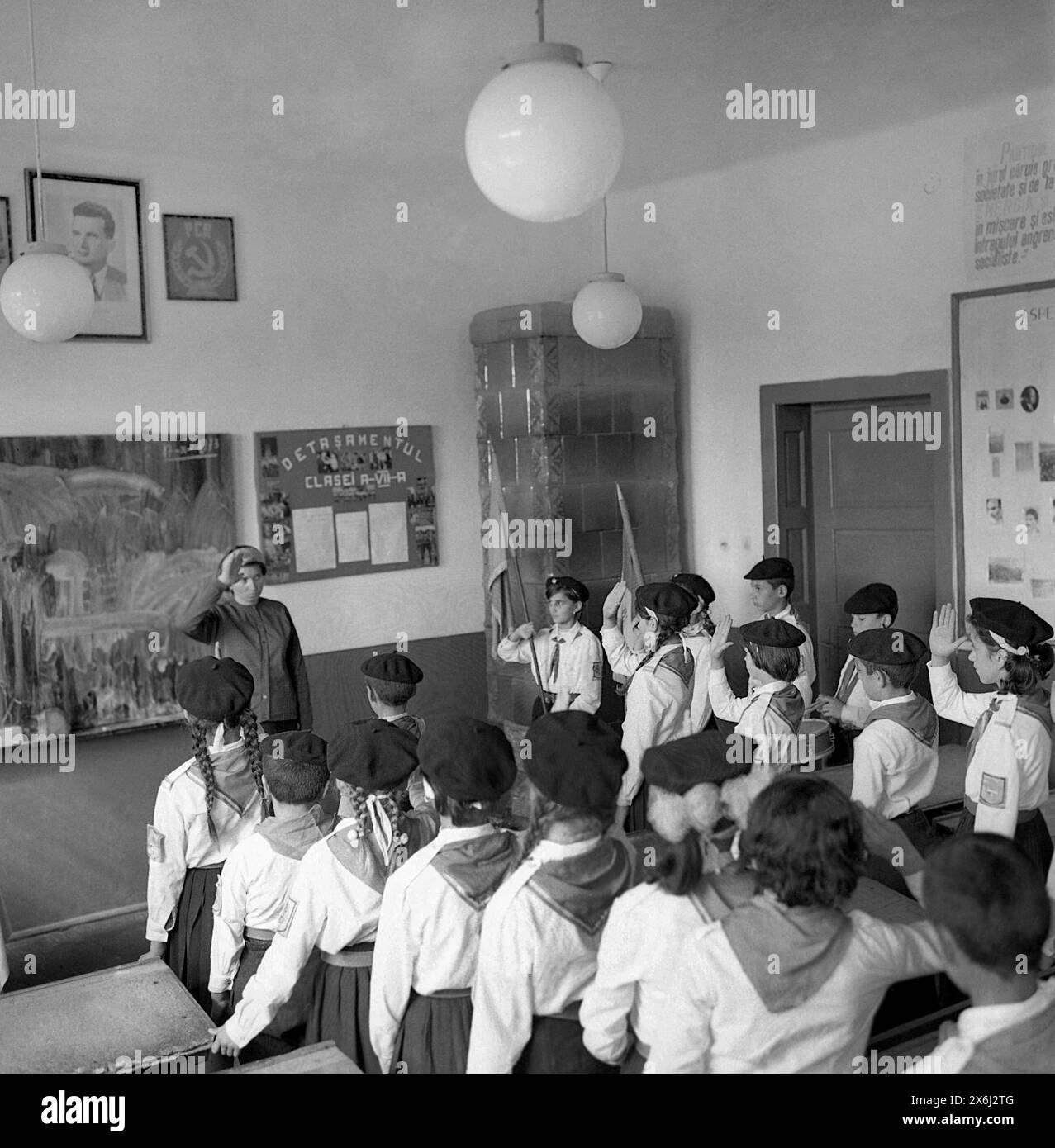 Socialist Republic of Romania in the 1970s. A classroom of 'Pioneers', students in middle school wearing the standardized uniform, performing the militaristic, propagandist ritual, which included the communist flag, the oath, and the salute. The communist symbols (the hammer and sickle) are displayed on the front wall. Stock Photo