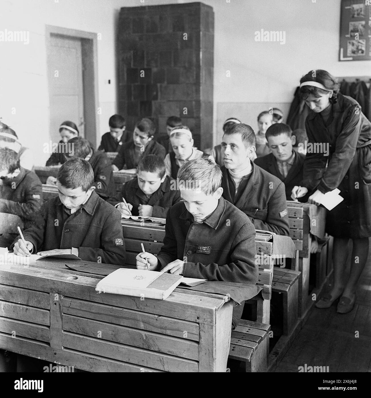 Șcheia, Suceava County, Socialist Republic of Romania  in the 1970s. 'Pioneers', students in middle school wearing the standardized communist uniform, during a class. This rural school had simple wooden furniture and a large terracotta wood stove for heating. Stock Photo