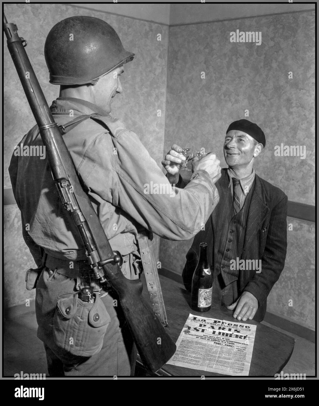 WW2 France Liberation August 1944 GI Pvt John Simms toasts  Frenchman, Mr Louis Lehaut, who is wearing a typical beret, with glasses of fine Cognac. A French newspaper in foreground with the news that Paris has been liberated from the Nazis. Cherbourg Normandy France Stock Photo