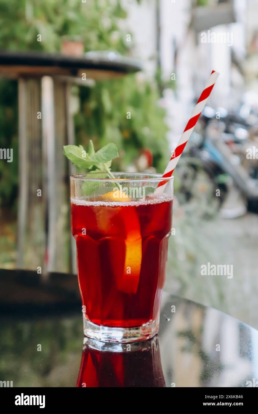 A glass of red drink (fruit iced tea) with a straw, on the terrace of a ...