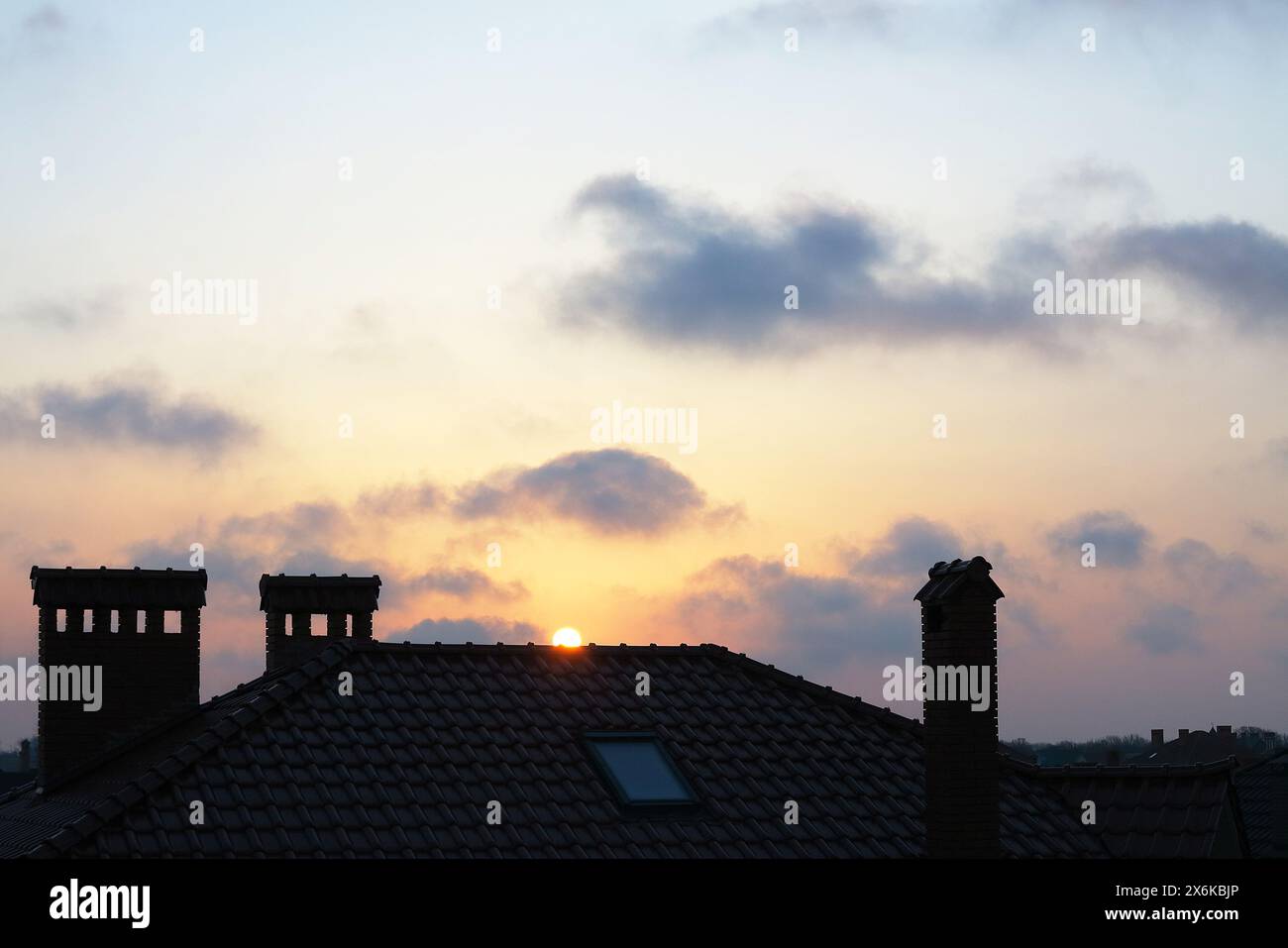 Chimneys, tiled roof of a house and beautiful clouds in the haze at sunset Stock Photo