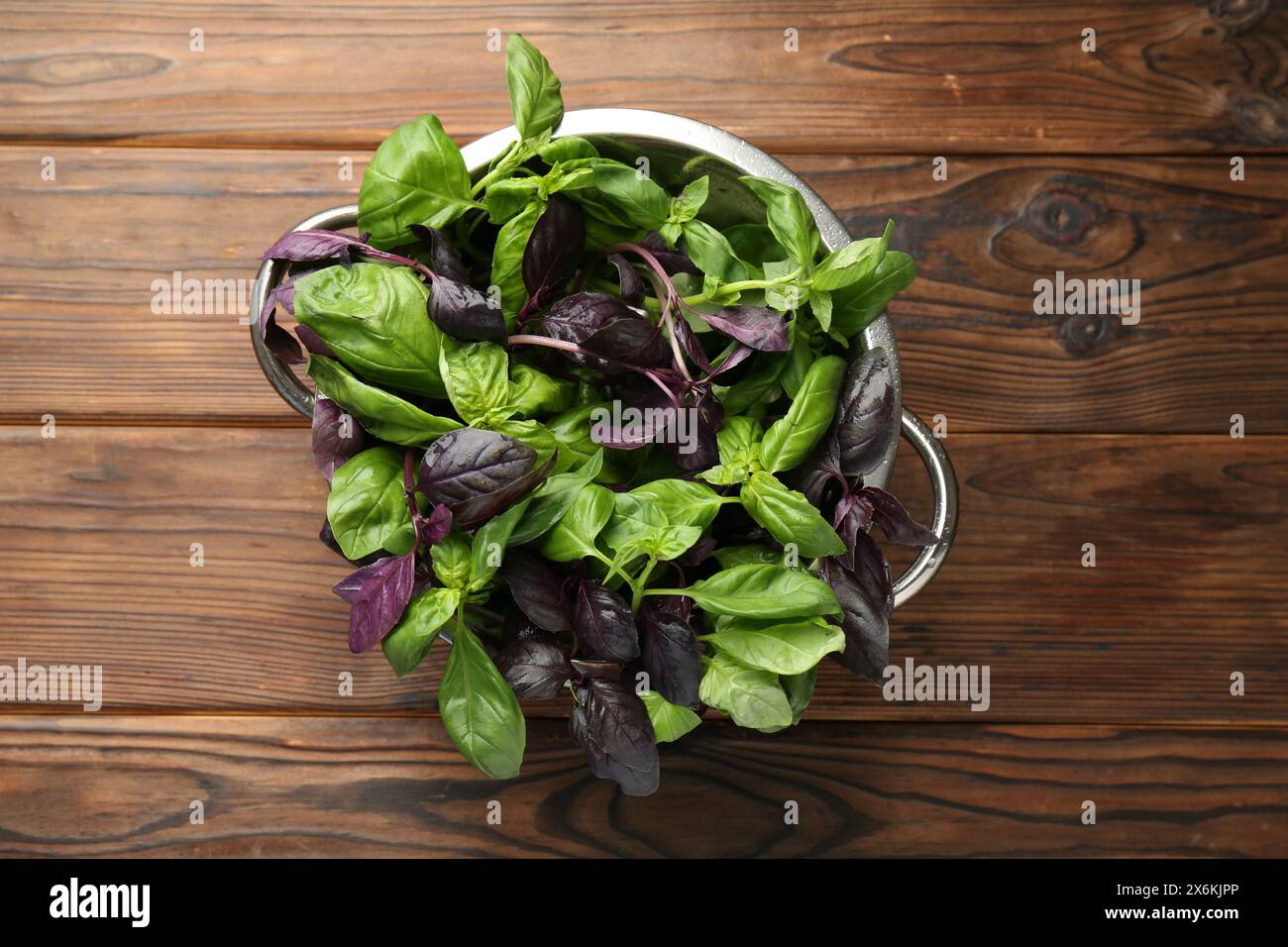 Metal colander with different fresh basil leaves on wooden table, top ...