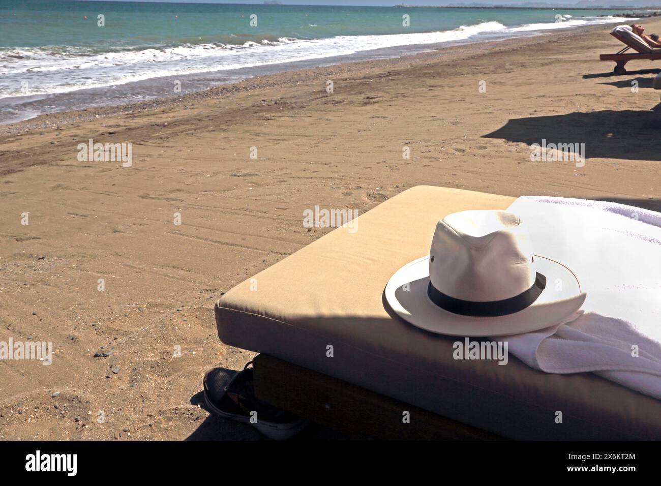 Sun Hat on Sun Lounger on Beach with Tourist Sunbathing in the Distance at The Chedi Hotel Beach Muscat Oman Stock Photo