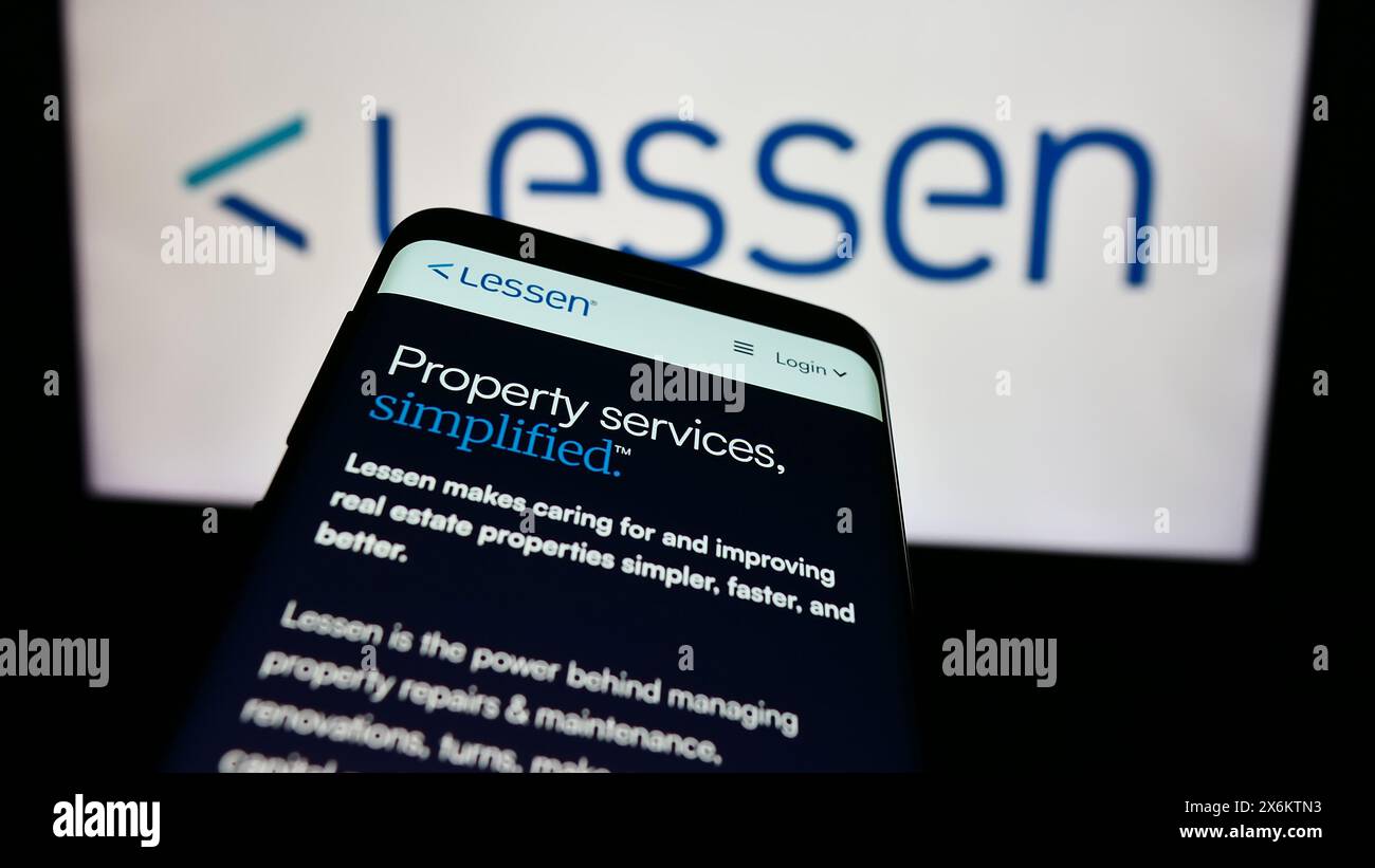 Mobile phone with website of US property services marketplace company Lessen Inc. in front of business logo. Focus on top-left of phone display. Stock Photo