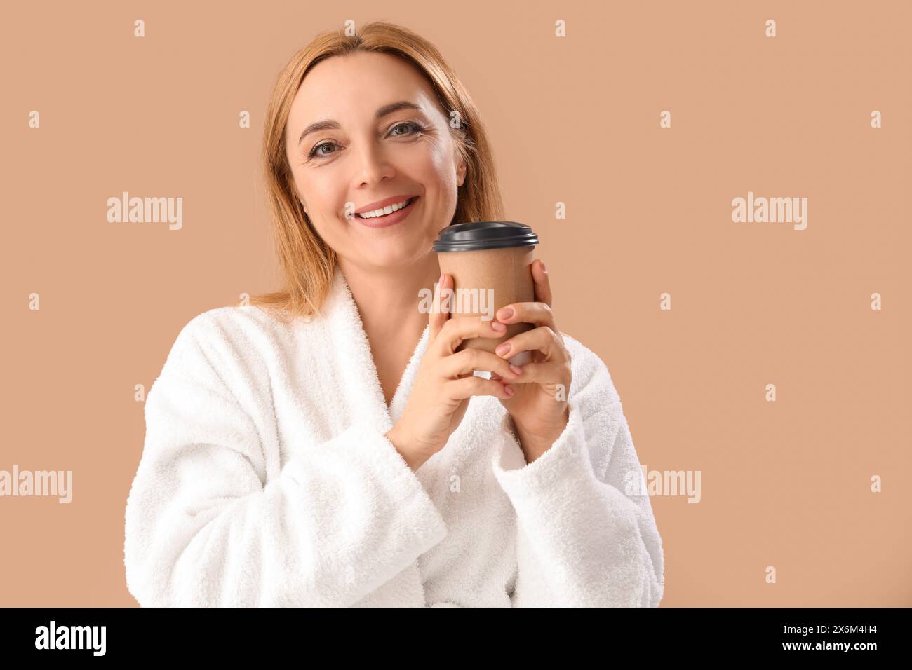 Mature woman in bathrobe with coffee cup on beige background Stock Photo