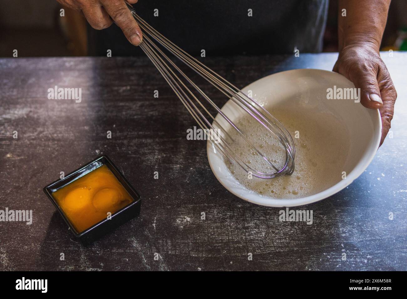 Baker's hands beating eggs with a hand mixer on a white plate
