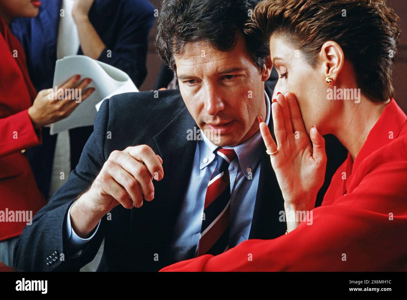 A male and female executive conferring buy whispering during a meeting Stock Photo