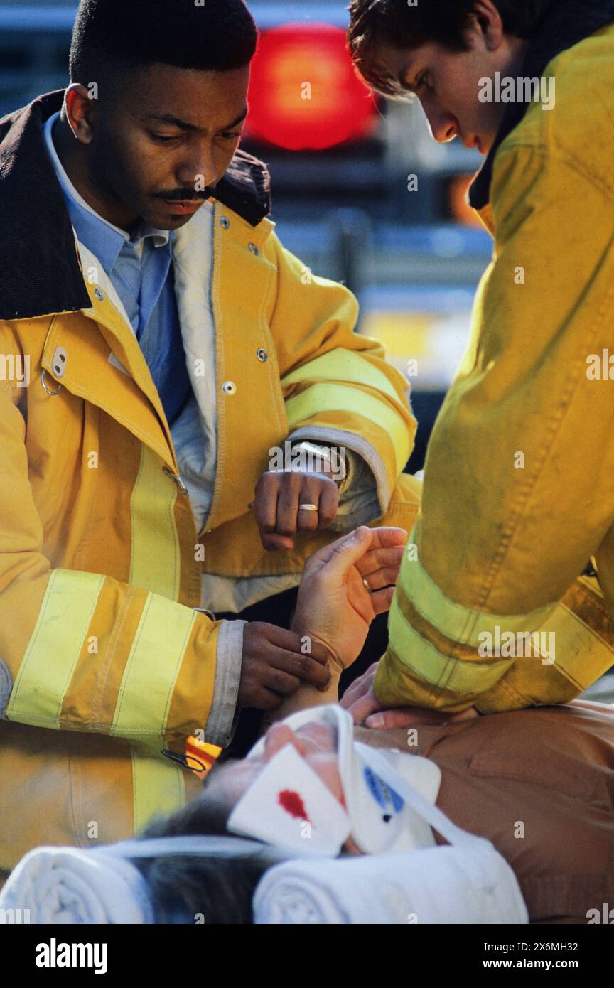 Two dedicated paramedics in yellow jackets provide urgent medical assistance to an injured individual on the street. Using a stethoscope and other ess Stock Photo