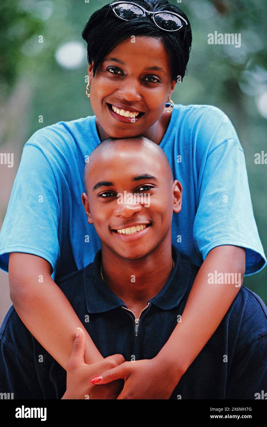 A black man and woman are striking a pose for a picture, smiling at the camera. They are standing close together, looking confident and happy. Stock Photo