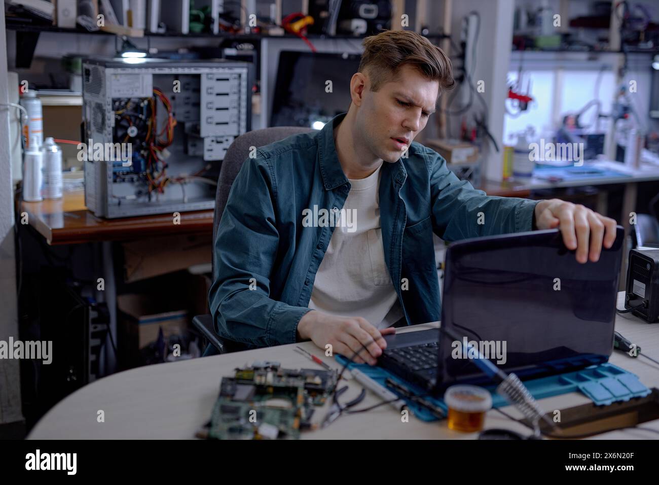 caucasian professional technician sit thinking how to repair fault laptop, sit behind table at workshop. Repairs and diagnostics breakdowns of laptop in professional service center. Stock Photo