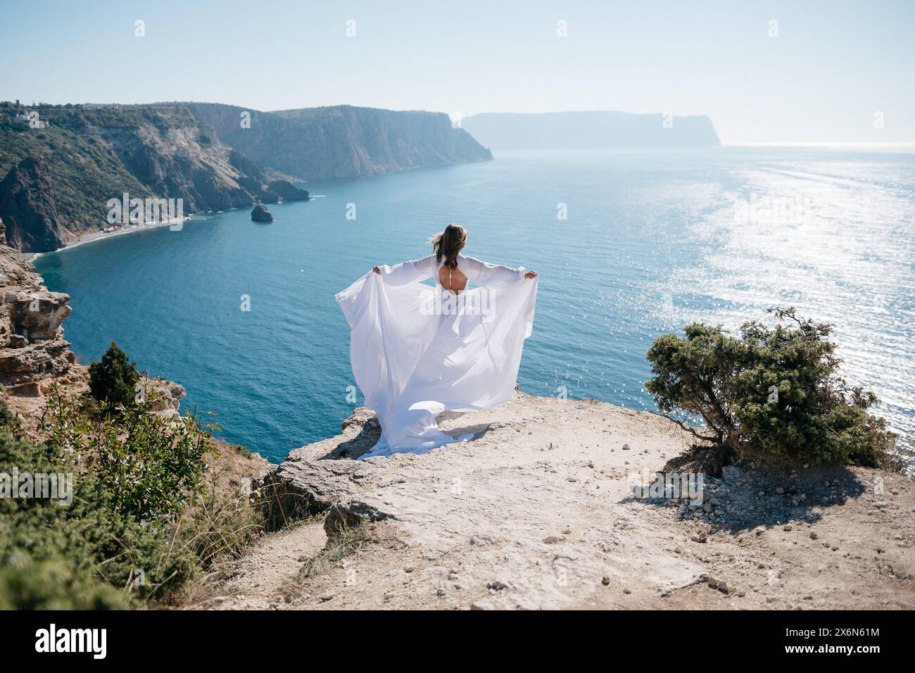 woman white dress stands on a rocky cliff overlooking the ocean. The ...