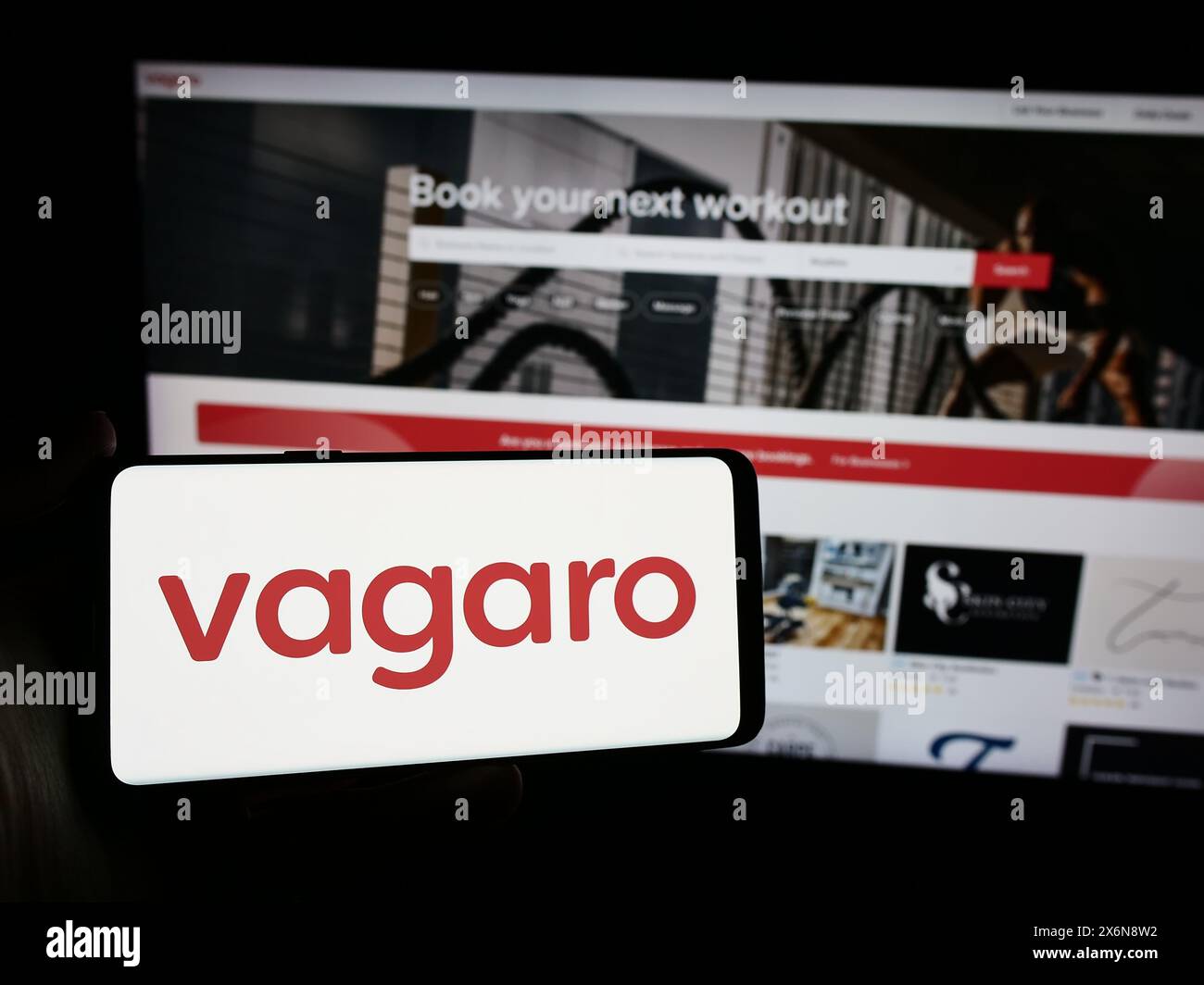 Person holding smartphone with logo of US wellness online marketplace company Vagaro Inc. in front of website. Focus on phone display. Stock Photo