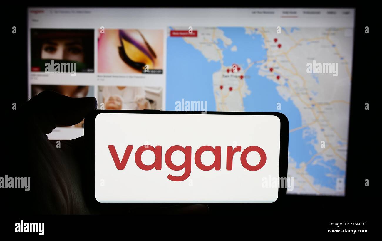 Person holding mobile phone with logo of American wellness online marketplace company Vagaro Inc. in front of web page. Focus on phone display. Stock Photo