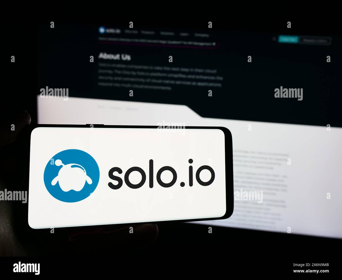 Person holding mobile phone with logo of American networking platform company Solo.io Inc. in front of business web page. Focus on phone display. Stock Photo