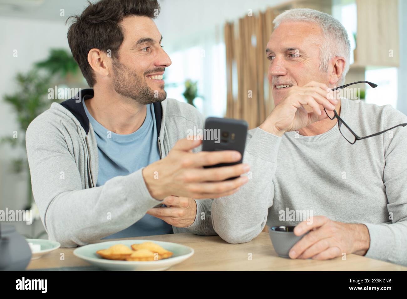 excited elderly dad and grown-up son browsing internet on smartphone Stock Photo
