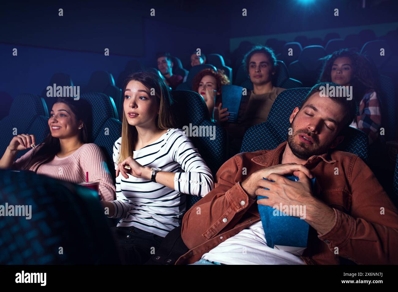 Group of people watching movie in cinema, girl wakes the sleeping boyfriend. Stock Photo