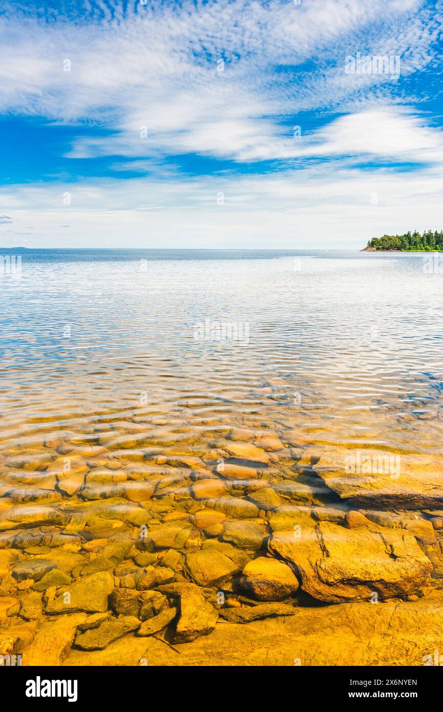 Lake Vänern in Sweden features clear, calm waters under a bright summer sky. The rocky shore adds texture and beauty to this serene scene. Stock Photo