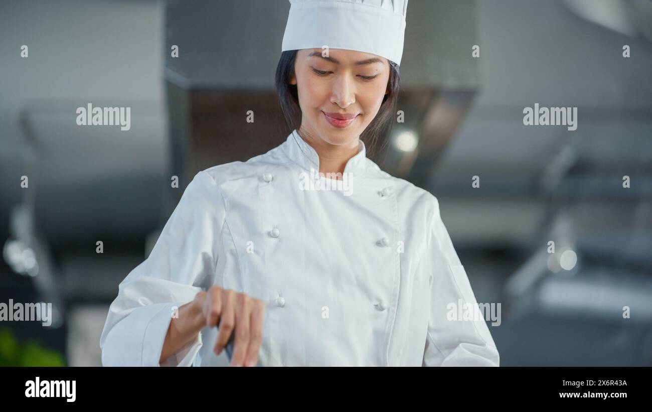 Restaurant Kitchen: Portrait of Asian Female Chef Stirs Her Favourite most Flavourful Dish, Smiles. Professional Cooking Delicious and Traditional Authentic Food. Healthy Dish Preparation. Low Angle Stock Photo