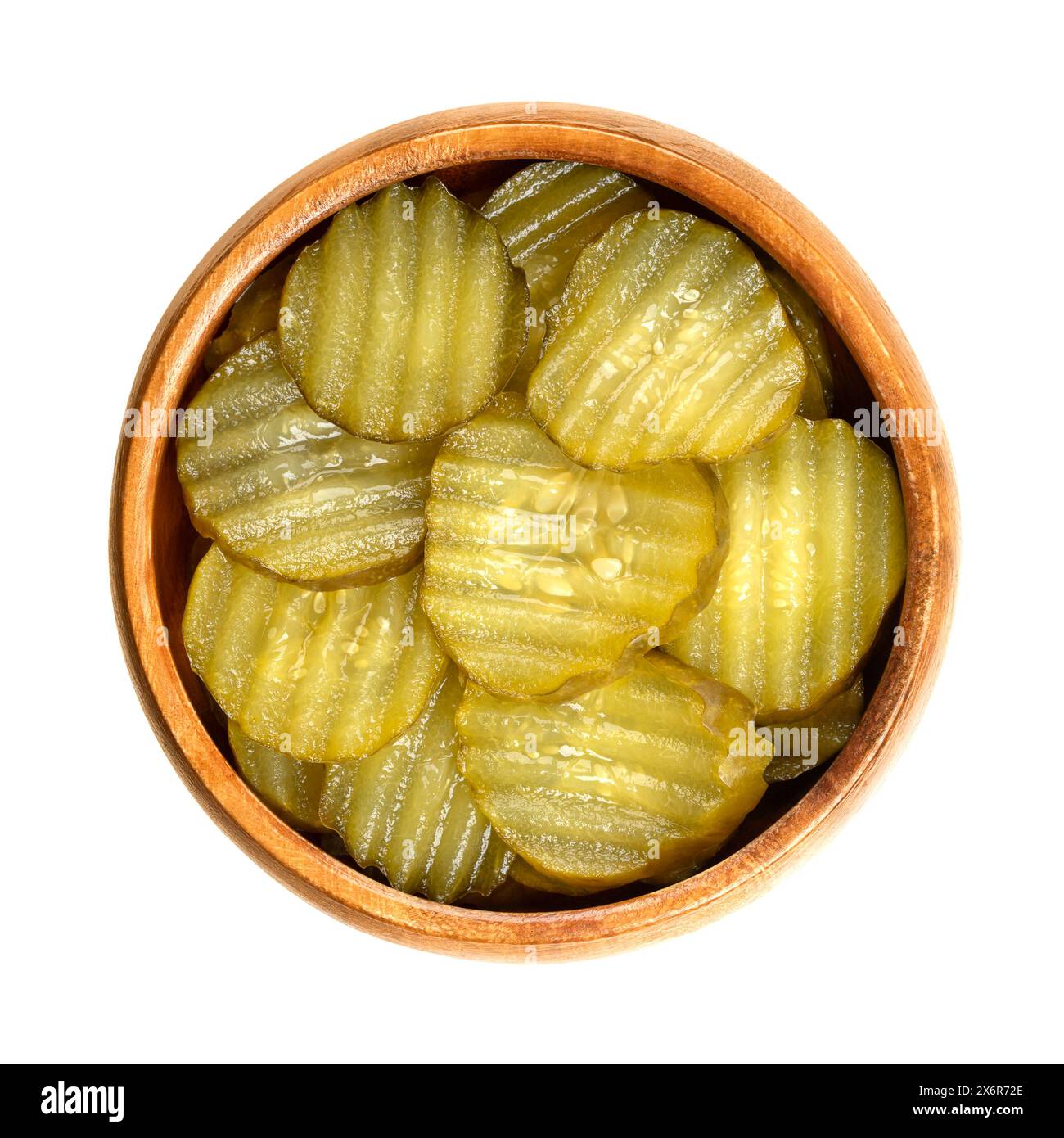 Burger gherkin slices, in a wooden bowl. Pickled cucumbers, cut in round and wavy form, pasteurized and preserved in vinegar brine, with spices. Stock Photo
