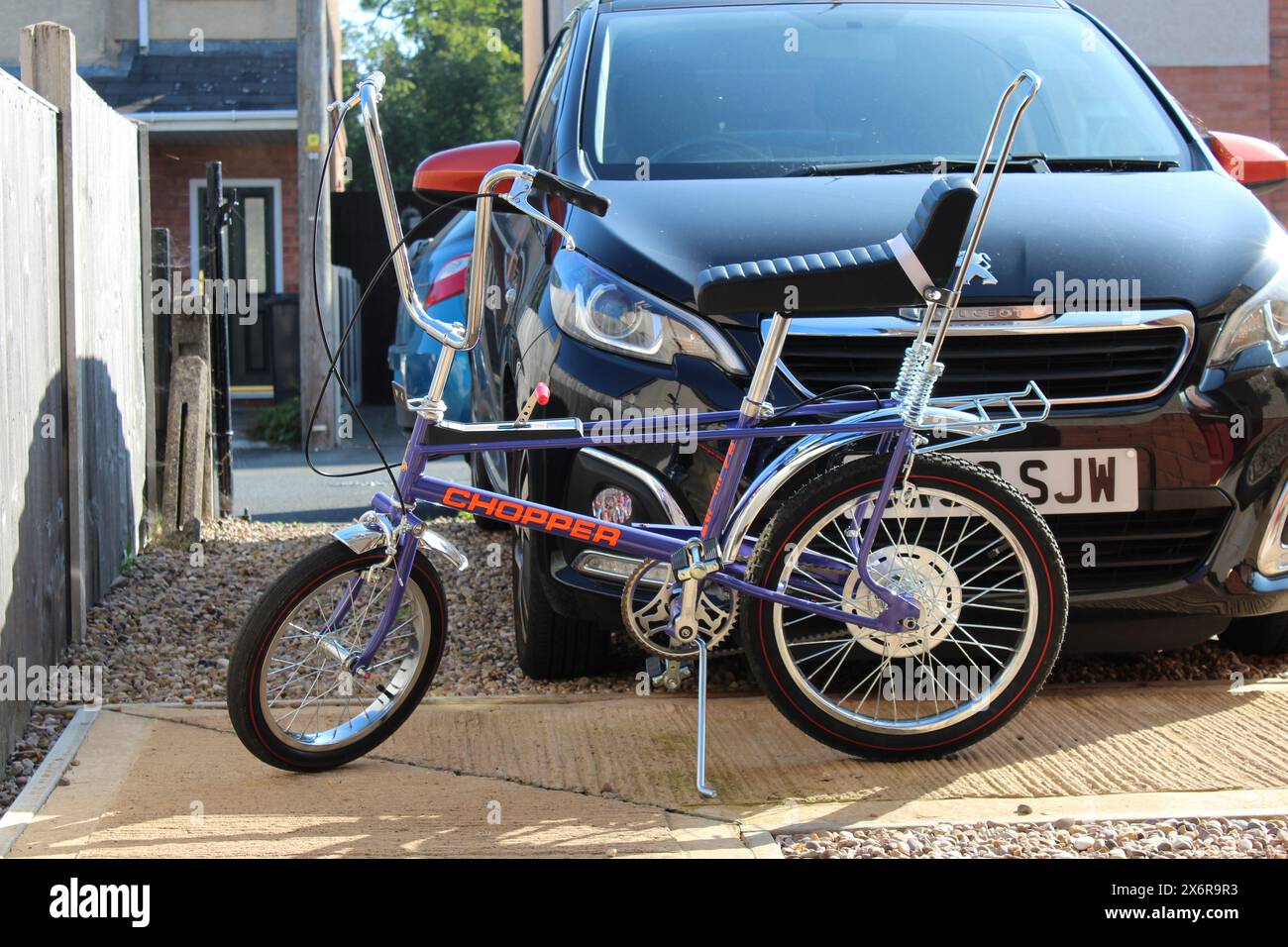 ultra violet raleigh chopper stood on its own on its stand in front of a car Stock Photo