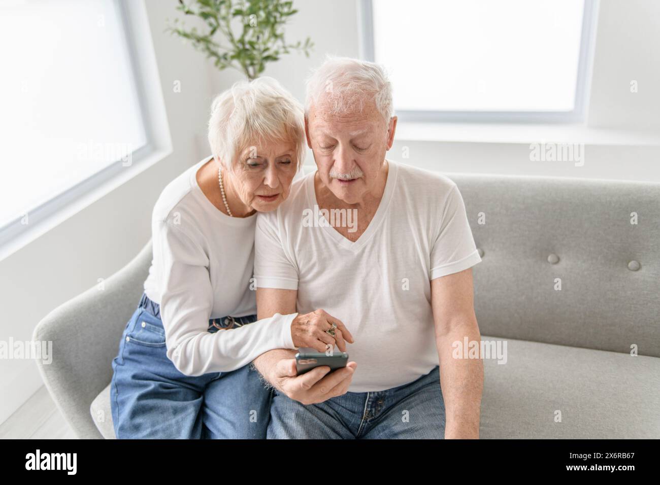 senior retired couple having great moment together on cozy sofa using cellphone Stock Photo