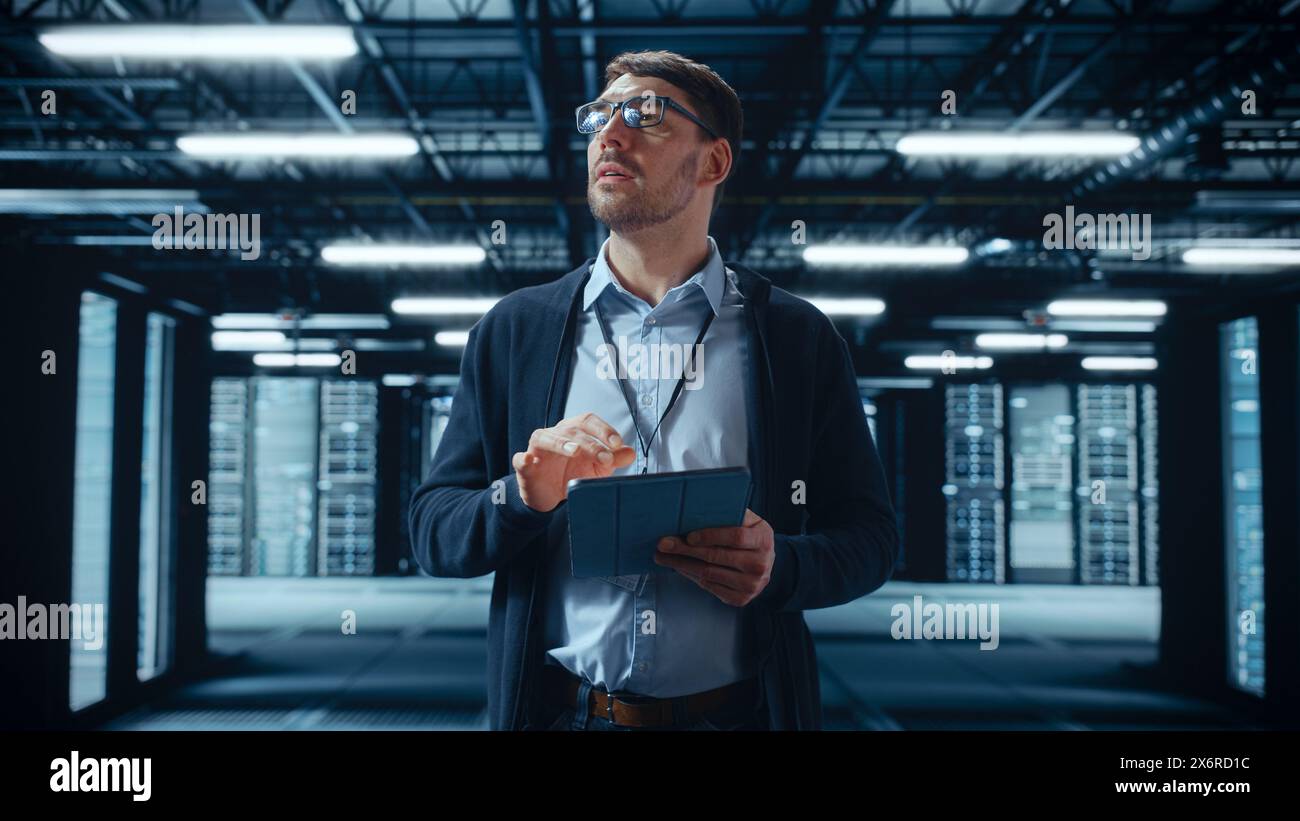 Male IT Specialist Walks Between Row of Operational Server Racks in Data Center. Engineer Uses Tablet Computer for Maintenance and Diagnostics in Cyber Security and Data Protection Facility. Stock Photo